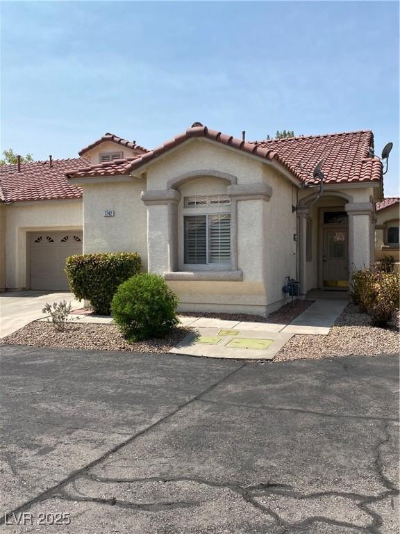 mediterranean / spanish house with a garage, driveway, a tiled roof, and stucco siding