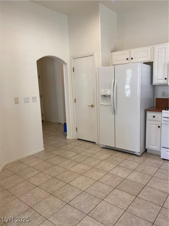 kitchen featuring arched walkways, light tile patterned floors, dark countertops, white cabinetry, and white appliances