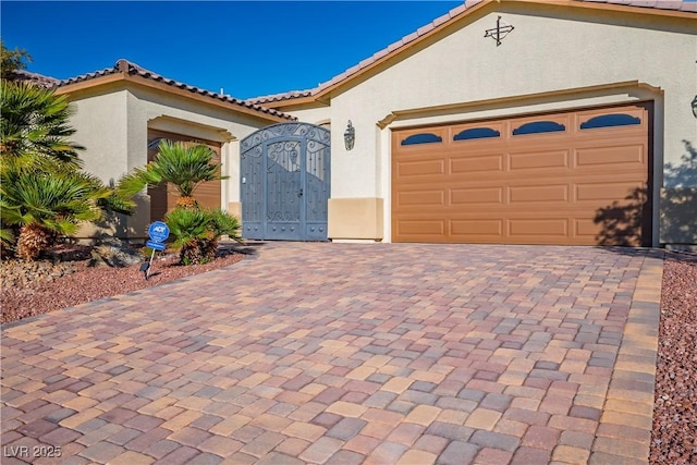 mediterranean / spanish-style house featuring a gate, stucco siding, a tiled roof, decorative driveway, and a garage