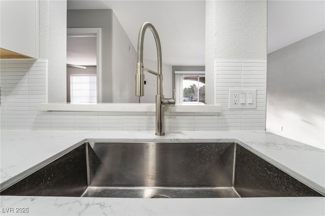 interior details featuring sink, backsplash, and light stone counters