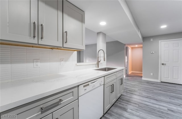 kitchen featuring a sink, white dishwasher, gray cabinetry, light wood-type flooring, and backsplash