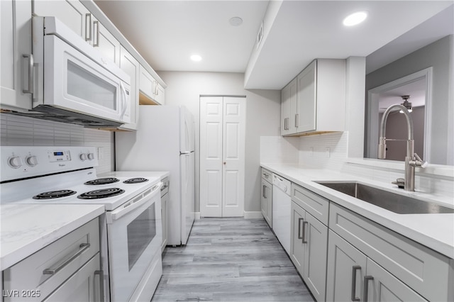 kitchen with sink, backsplash, white appliances, and light wood-type flooring