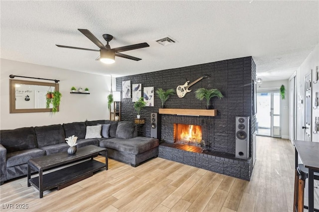 living room featuring hardwood / wood-style floors, a textured ceiling, ceiling fan, and a brick fireplace