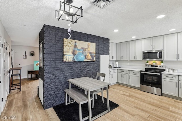 kitchen with light hardwood / wood-style flooring, white cabinetry, a textured ceiling, decorative light fixtures, and stainless steel appliances