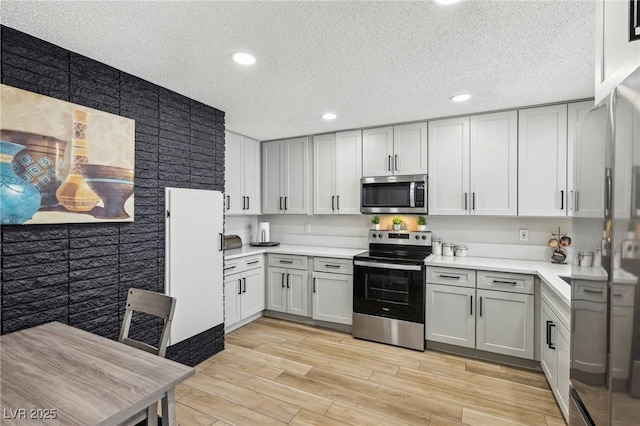 kitchen with a textured ceiling, stainless steel appliances, and light hardwood / wood-style flooring