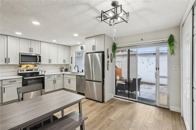 kitchen featuring white cabinetry, stainless steel appliances, decorative light fixtures, light hardwood / wood-style floors, and sink