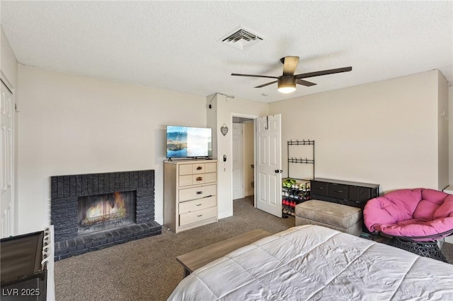 bedroom featuring dark carpet, ceiling fan, a brick fireplace, and a textured ceiling