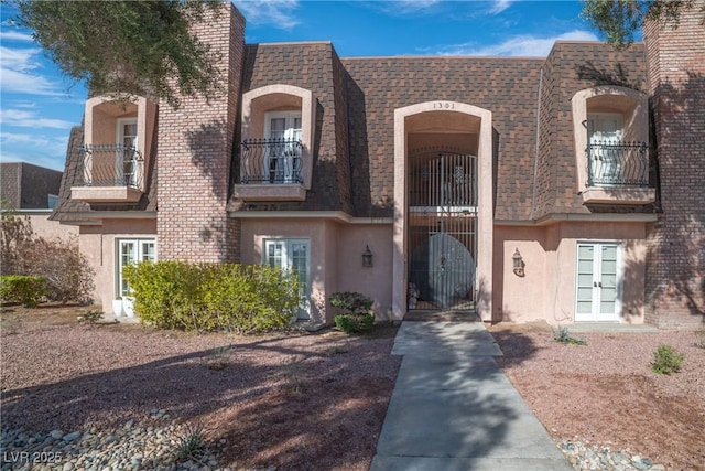 view of front of property featuring french doors, roof with shingles, stucco siding, a gate, and a balcony