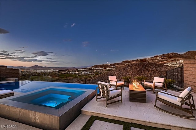 pool at dusk featuring a mountain view, a patio, an in ground hot tub, and fence