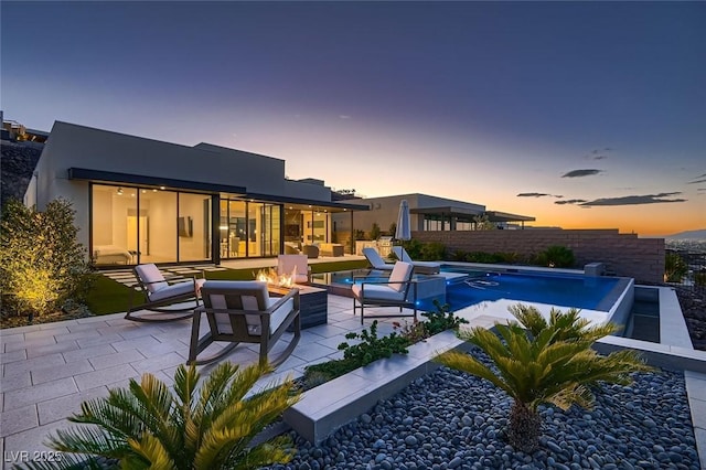 back of property at dusk featuring a fenced in pool, a fire pit, fence, stucco siding, and a patio area