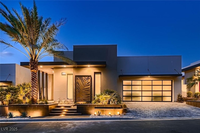 contemporary house with decorative driveway, a garage, and stucco siding