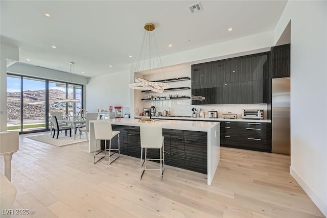 kitchen featuring visible vents, modern cabinets, stainless steel fridge, a breakfast bar area, and light countertops