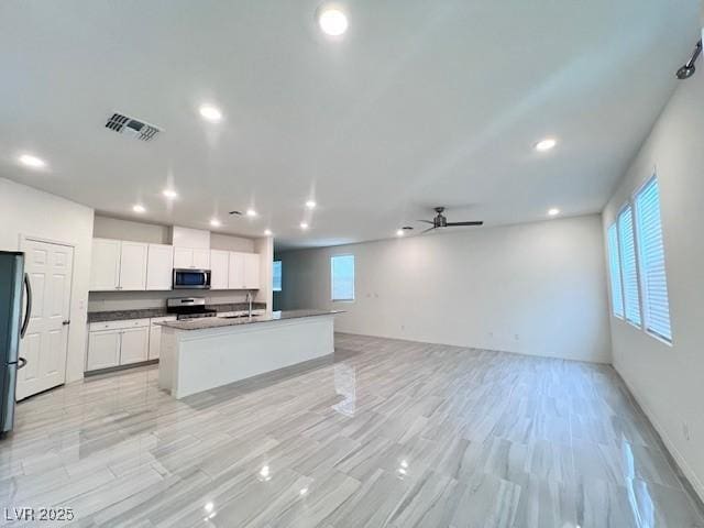 kitchen with an island with sink, white cabinetry, stainless steel appliances, and a wealth of natural light