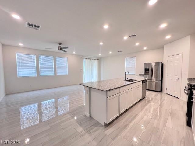 kitchen featuring a center island with sink, sink, light stone counters, stainless steel appliances, and white cabinets