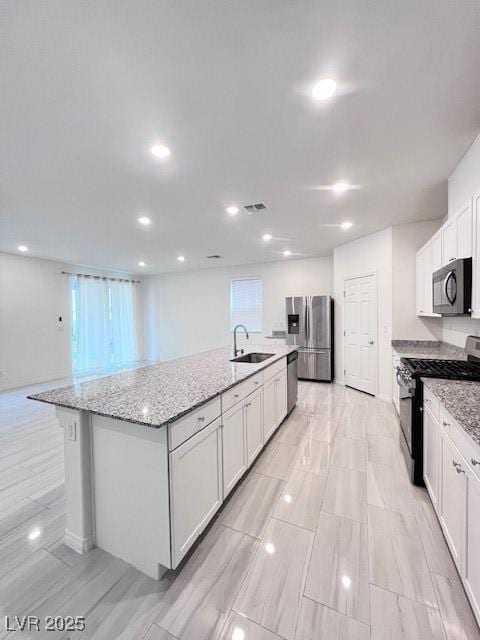 kitchen with white cabinetry, a kitchen island with sink, light stone countertops, sink, and appliances with stainless steel finishes