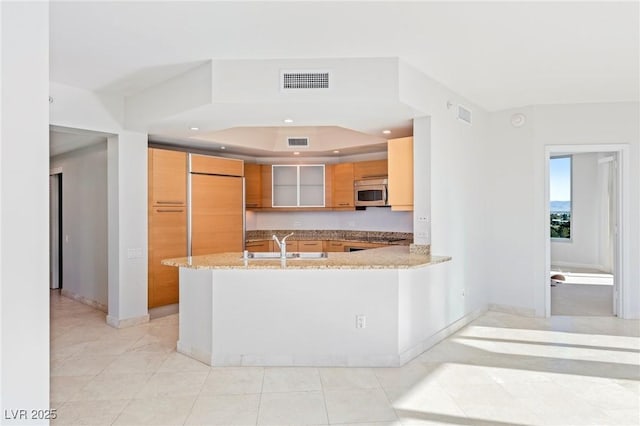 kitchen with kitchen peninsula, built in fridge, sink, light stone counters, and light tile patterned flooring