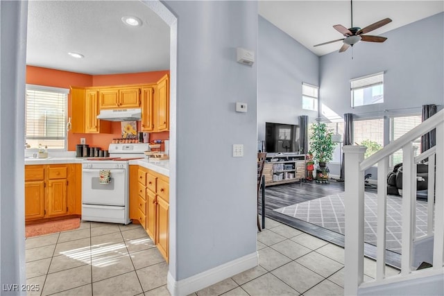 kitchen featuring light tile patterned floors, ceiling fan, white range, and a towering ceiling