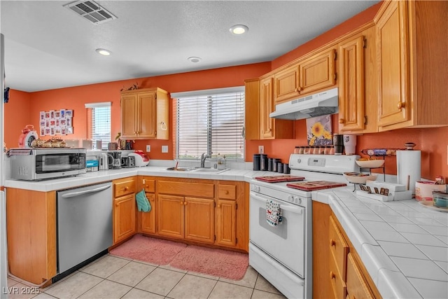 kitchen featuring sink, tile countertops, appliances with stainless steel finishes, and light tile patterned flooring