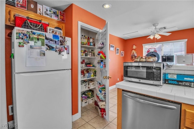 kitchen featuring tile counters, tasteful backsplash, ceiling fan, light tile patterned floors, and appliances with stainless steel finishes