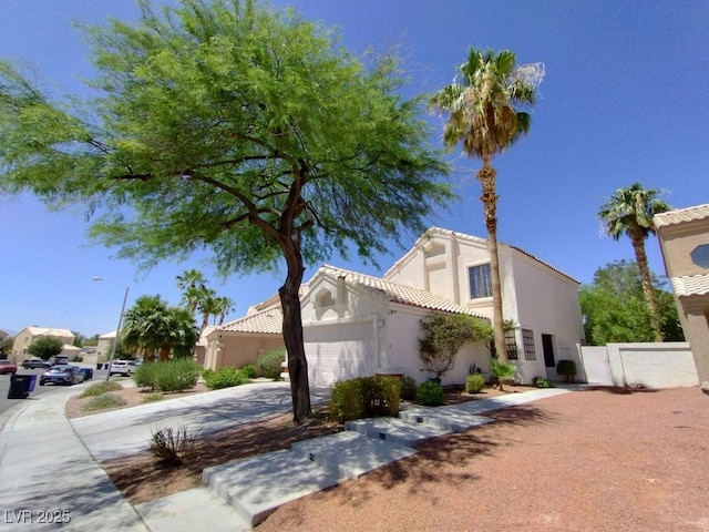 view of side of home with a garage, a tile roof, concrete driveway, a gate, and stucco siding