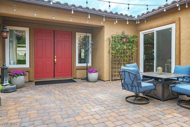 entrance to property featuring outdoor dining space, a tile roof, a patio, and stucco siding