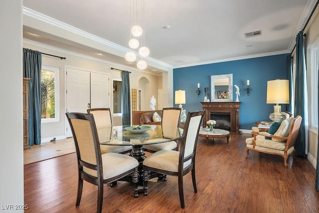 dining area featuring crown molding, arched walkways, a fireplace, and wood finished floors