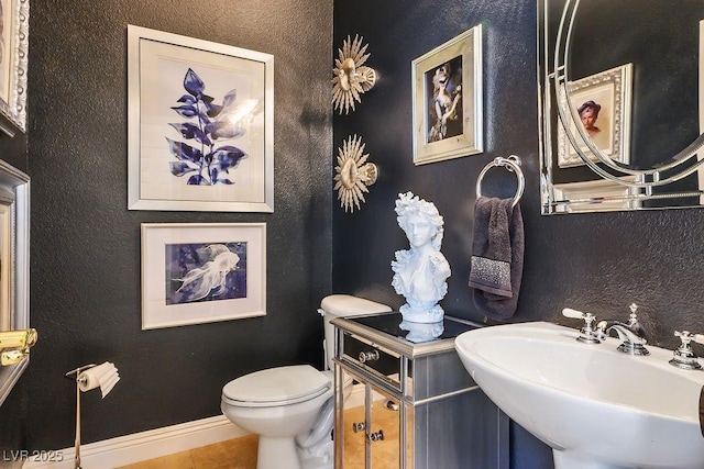 bathroom featuring a textured wall, a sink, toilet, and baseboards