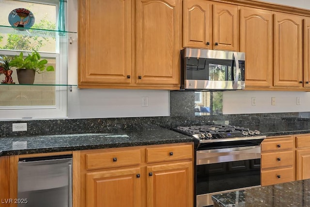 kitchen with brown cabinetry, stainless steel appliances, and dark stone countertops