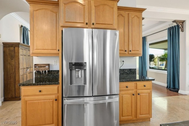 kitchen with arched walkways, baseboards, dark stone counters, stainless steel fridge, and crown molding