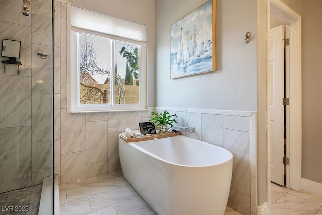 full bath featuring a freestanding bath, marble finish floor, and tile walls