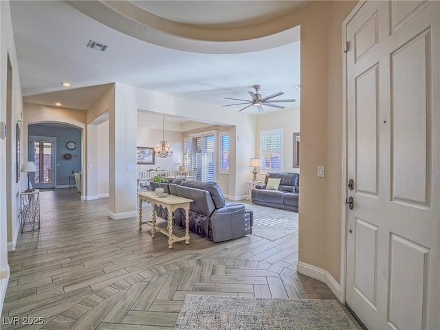 foyer entrance with ceiling fan with notable chandelier and light parquet flooring