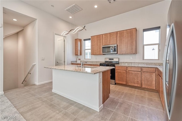 kitchen featuring appliances with stainless steel finishes, sink, light stone counters, light tile patterned flooring, and an island with sink