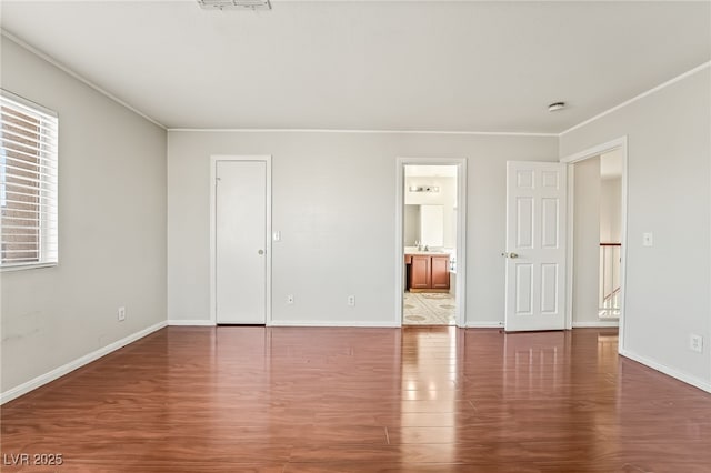 unfurnished bedroom featuring ornamental molding, dark wood-style flooring, a sink, and baseboards