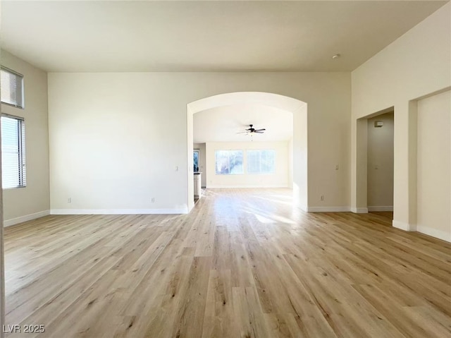 unfurnished living room with light wood-type flooring, arched walkways, and baseboards