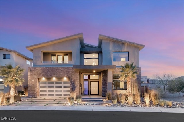 contemporary home with a balcony, a garage, driveway, stone siding, and stucco siding