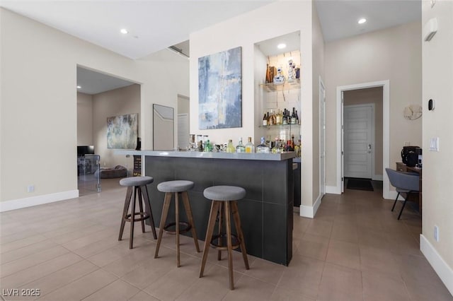 bar featuring a bar, tile patterned floors, baseboards, and recessed lighting