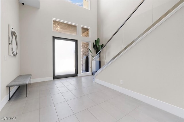 entryway featuring light tile patterned floors, a high ceiling, stairway, and baseboards