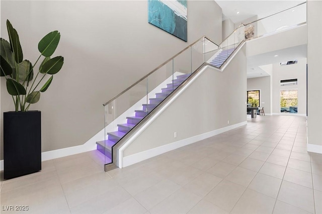 stairs featuring a high ceiling, tile patterned flooring, and baseboards