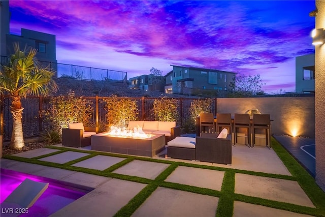 patio terrace at dusk featuring outdoor dry bar, an outdoor living space with a fire pit, and fence