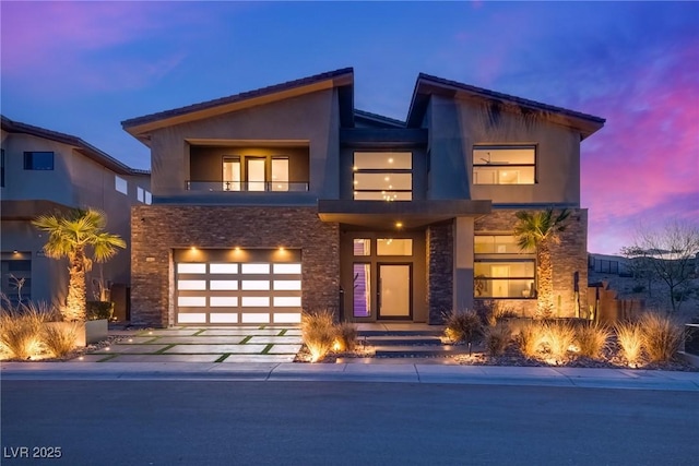 contemporary house with driveway, stone siding, a garage, and stucco siding