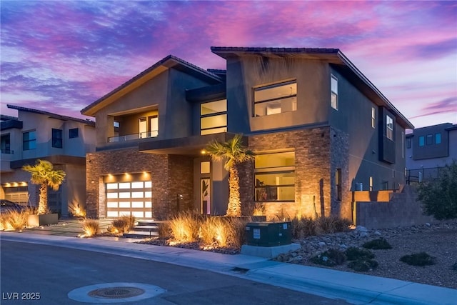 contemporary home featuring a garage, stone siding, a balcony, and stucco siding