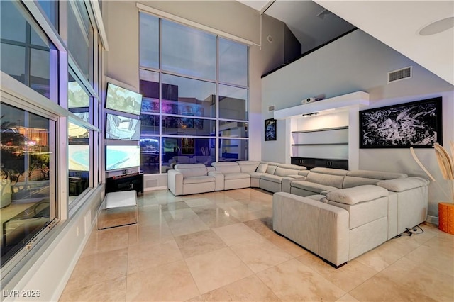 living area with tile patterned flooring, visible vents, and a towering ceiling