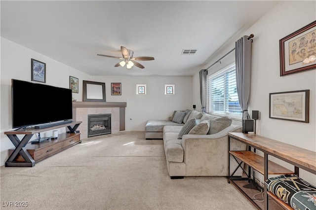 living room featuring light carpet, a tiled fireplace, and ceiling fan