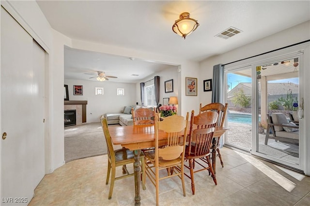 dining space featuring a tile fireplace, ceiling fan, and light tile patterned flooring