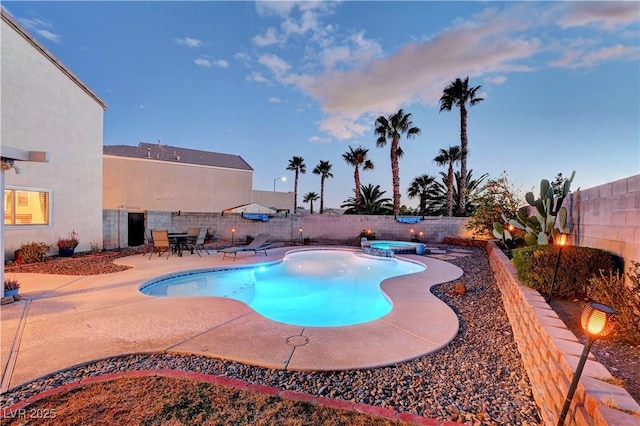 pool at dusk with a patio area and an in ground hot tub