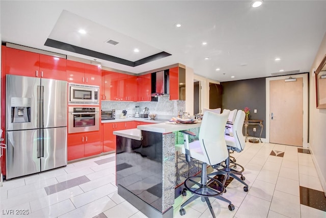 kitchen with stainless steel appliances, backsplash, a raised ceiling, a breakfast bar area, and wall chimney exhaust hood