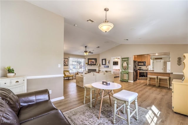 living room featuring light hardwood / wood-style floors, vaulted ceiling, and ceiling fan