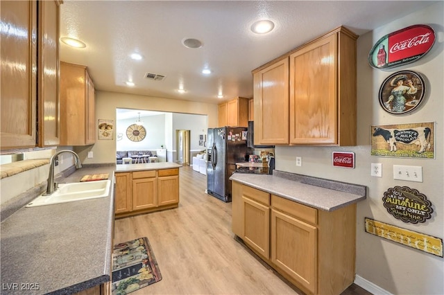 kitchen featuring sink, light wood-type flooring, pendant lighting, black fridge, and kitchen peninsula