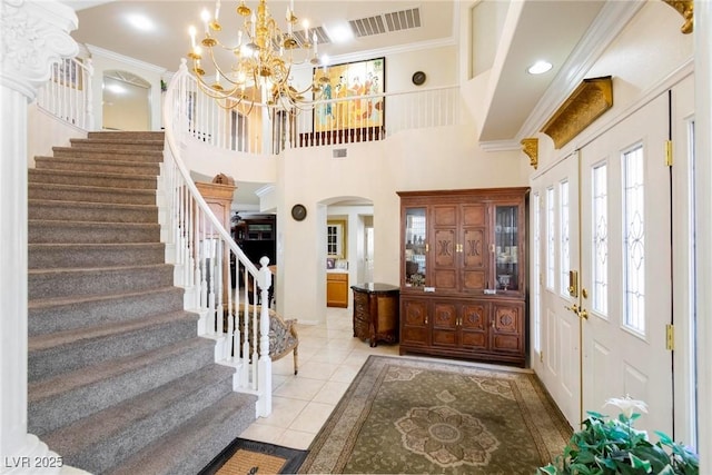 entryway with a high ceiling, ornamental molding, light tile patterned flooring, and a notable chandelier