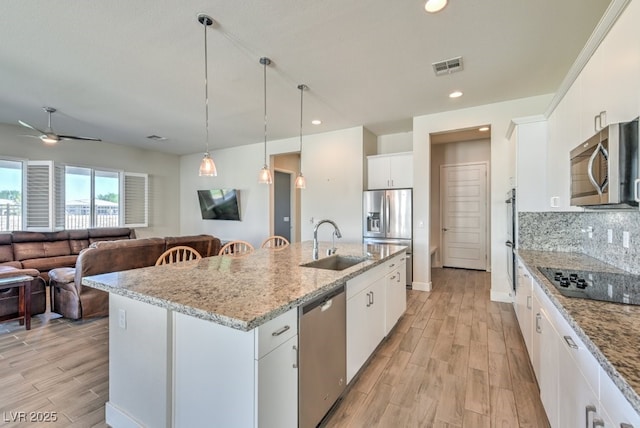 kitchen with an island with sink, stainless steel appliances, hanging light fixtures, sink, and white cabinets